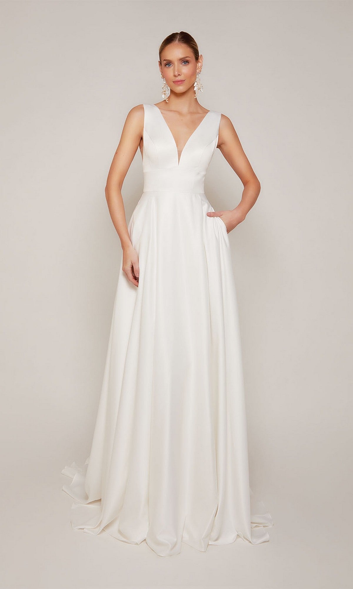 A woman poses against a plain light background in the Alyce 7096, a sleeveless, floor-length white satin formal dress with a deep V-neckline and subtle pleats.